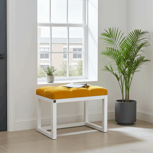 Wooden-framed velvet bench in bold yellow mustard with white frame, featuring button tufting, placed near a window with a potted plant, enhancing contemporary Irish interior design.