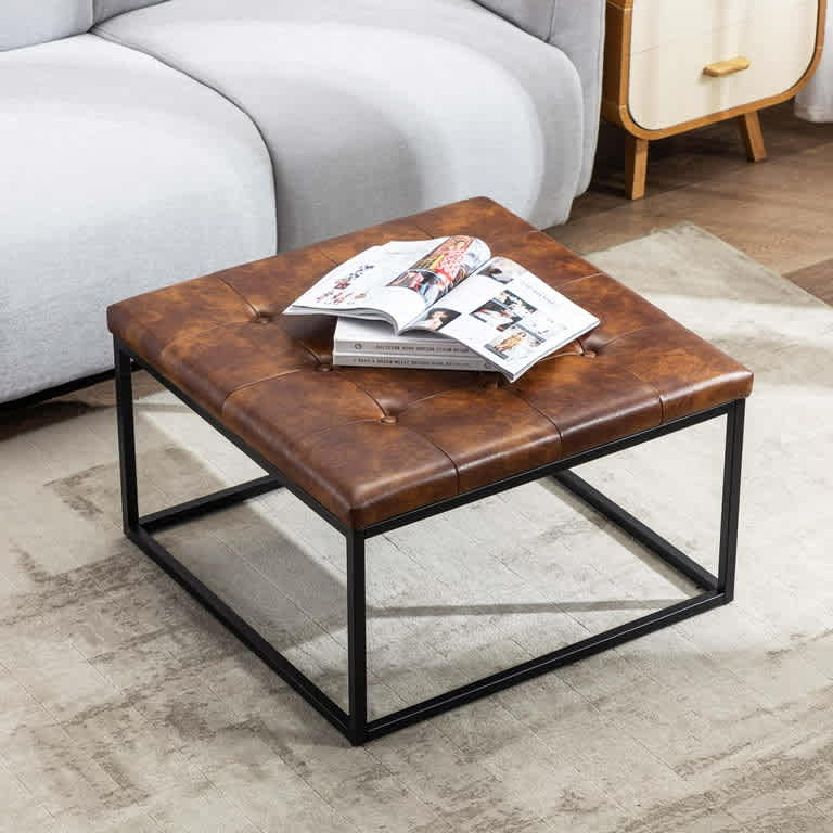 Modern square coffee table with a tufted brown faux leather top and a sleek black metal base, enhancing a contemporary living room