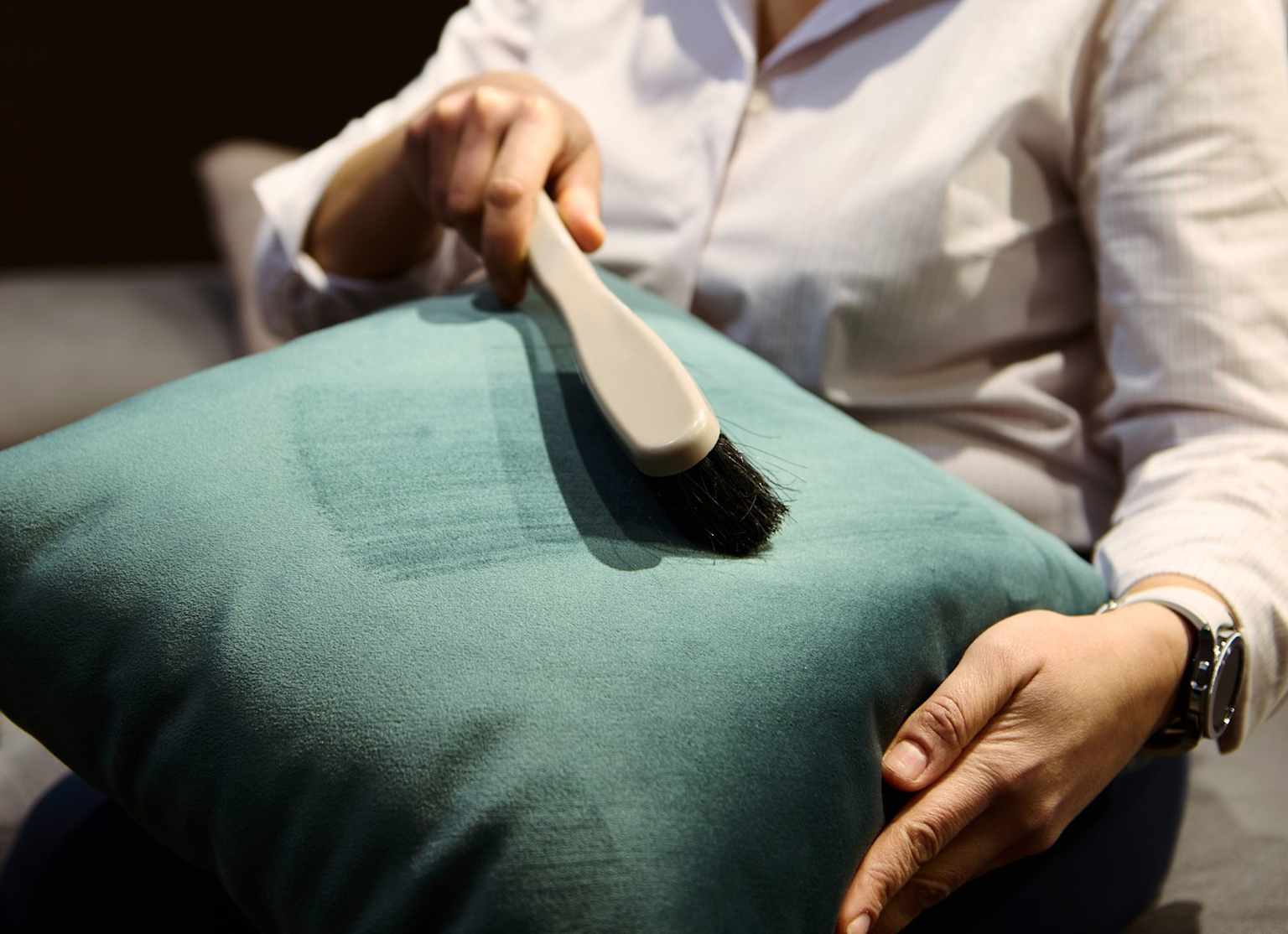 Person gently cleaning a teal velour cushion with a soft brush to maintain upholstery