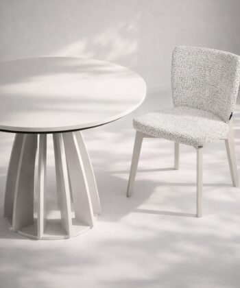 Modern white round table with a textured fabric chair in a minimalist setting.
