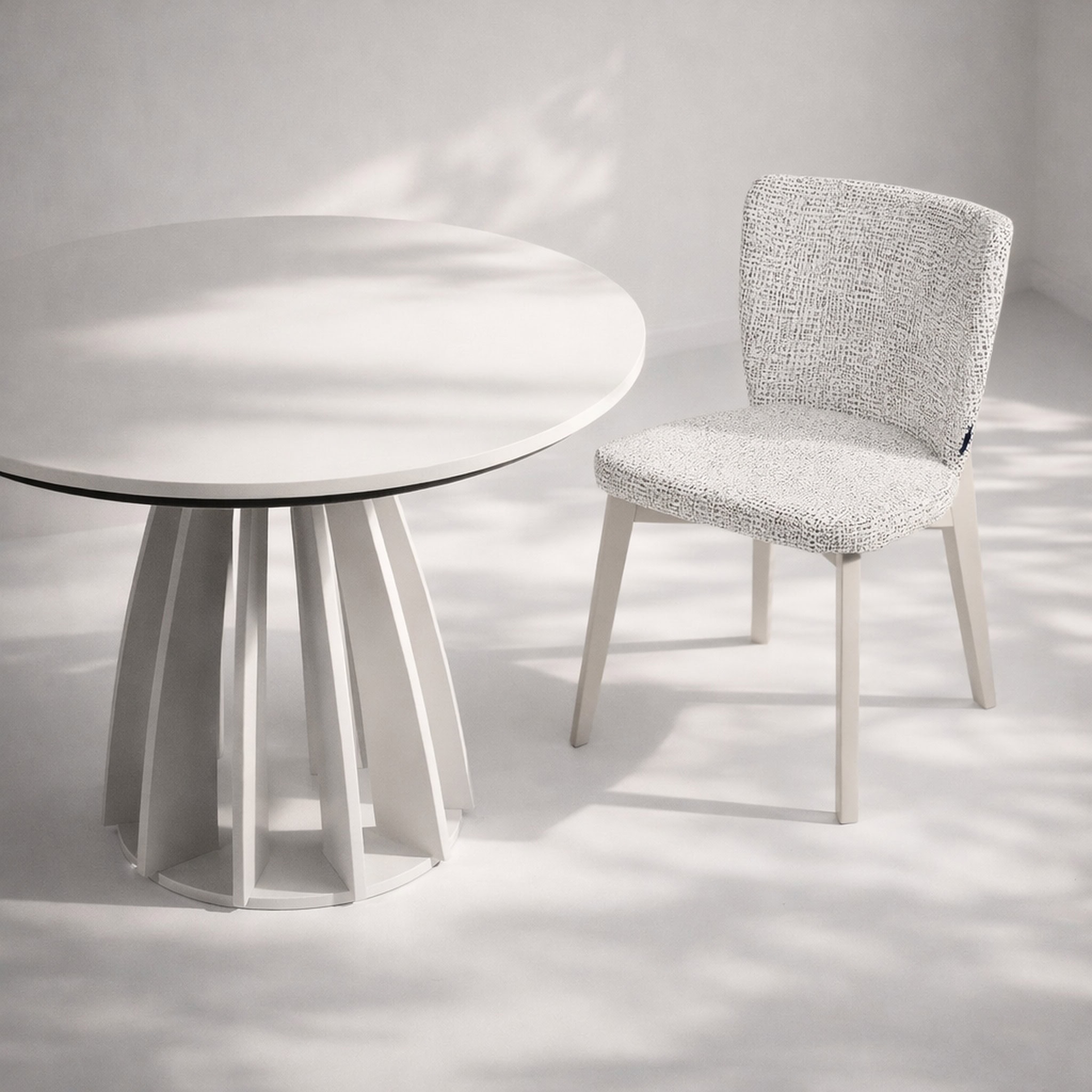Modern white round table with a textured fabric chair in a minimalist setting.