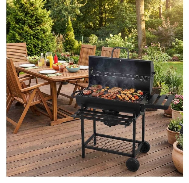 BBQ grill on a wooden patio with outdoor dining table and garden in the background.